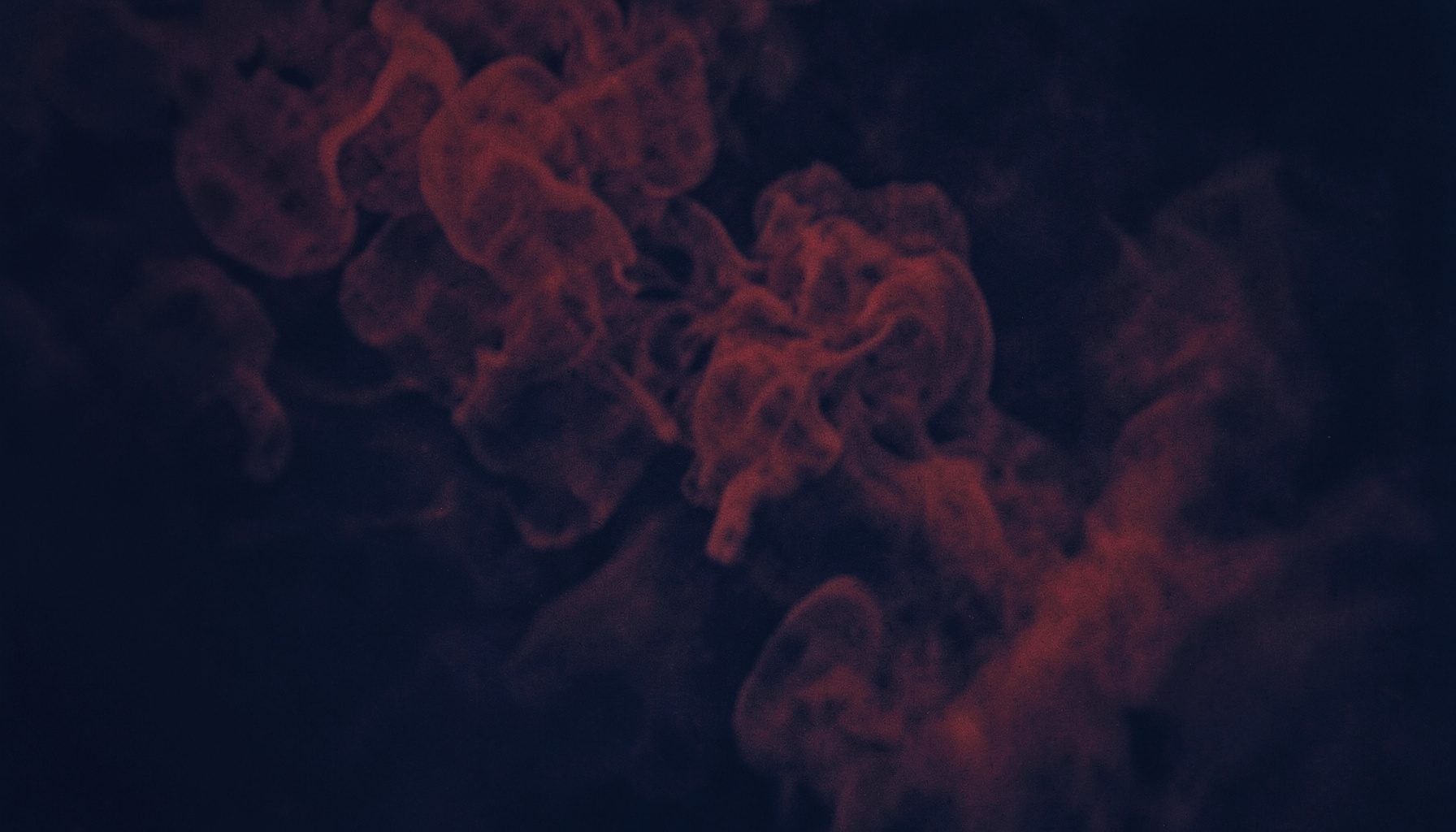 A dark atmospheric duotone photograph in deep navy and muted crimson tones, showing wisps of tobacco smoke drifting across a moody, shadowed backdrop with subtle texture